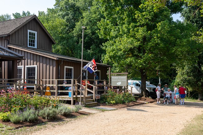 A wide gravel path in front of a two-story wood building with a front porch and a visitor center sign.