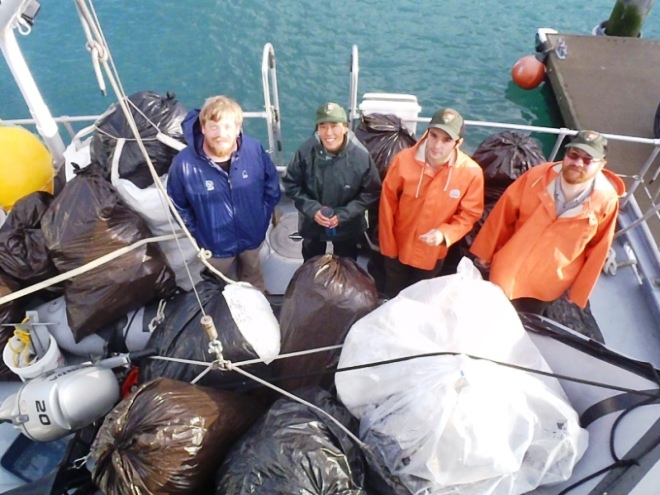 Four park staff stand of the deck of the park's boat, surrounded by the bags of garbage collected. 