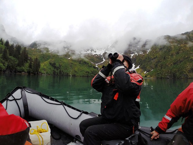 A park tech sits on the edge of a inflatable boat, while looking up through binoculars.