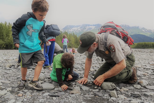 A park ranger talks to two children as they look at a rocky ground.