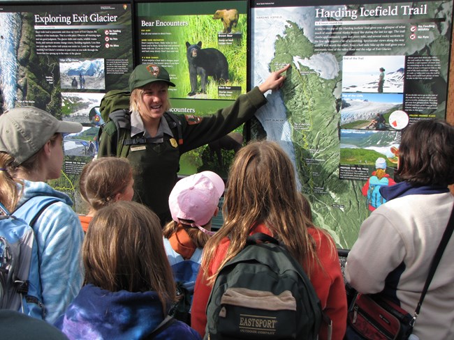 A park ranger talks to a group of students in front of an information panel about the Harding Icefield