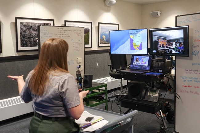 A ranger stands in front of multiple screens for distance learning.