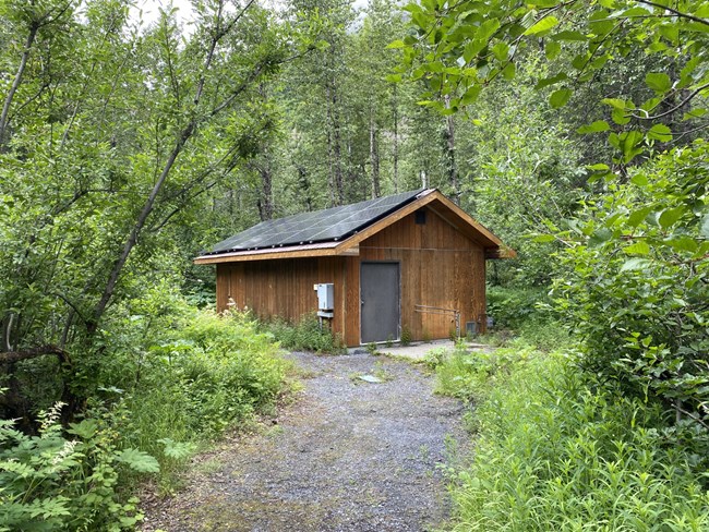 A brown building with solar panels at the end of a road surrounded by a green forest