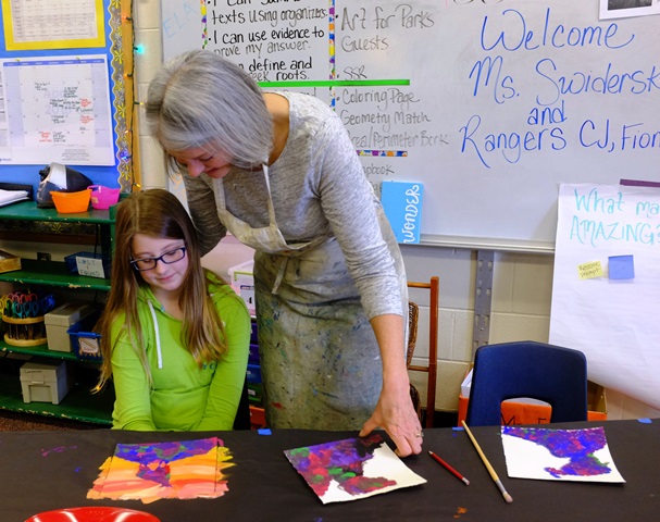 An older woman and young girl look at a watercolor the girl painted.