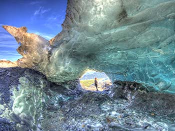 A woman stands in a hole in Exit Glacier with sunlit blue ice surrounding her.
