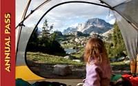 The image of the 2014 Annual pass show a young girl looking out her tent at a mountain in the distance.