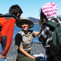 A park ranger holds up a jar of sea water to two children.