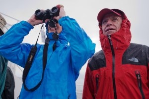 Two visitors stand on a tour boat, dressed in heavy rain gear.
