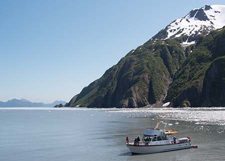 A boat sits in the water in front of a steep cliffl, while people put a kayak in the water.