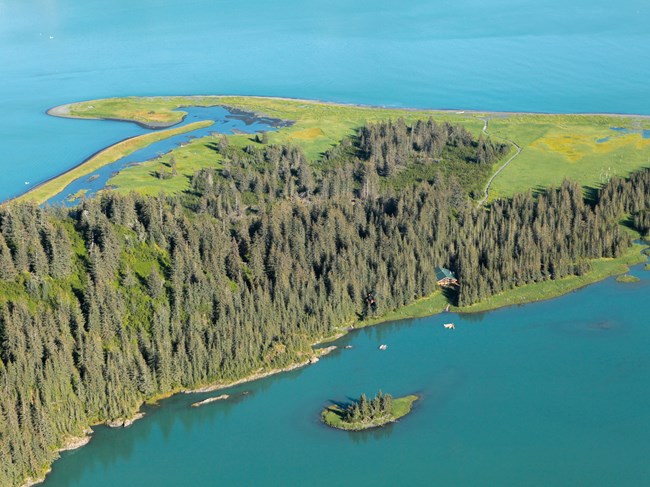 An aerial photo of a lodge on forested land surrounded by water