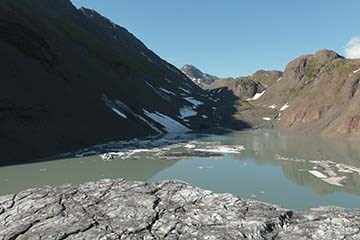 Small lake bordered by steep cliffs in the background and glacial ice in foreground.