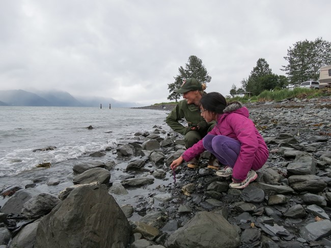 A park ranger and kid look out at water