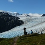 Two hikers stand on a trail, overlooking Exit Glacier as it flows out of the Harding Icefield.