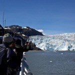 Two visitors take pictures of a tidewater glacier from the deck of a tour boat.