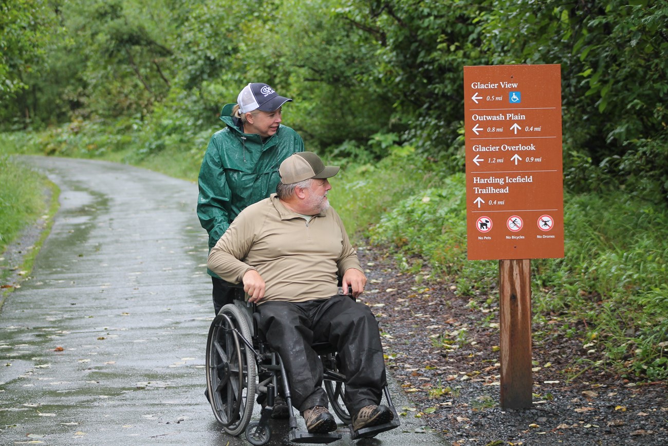 Two visitors, one in wheelchair, read trail sign for directions