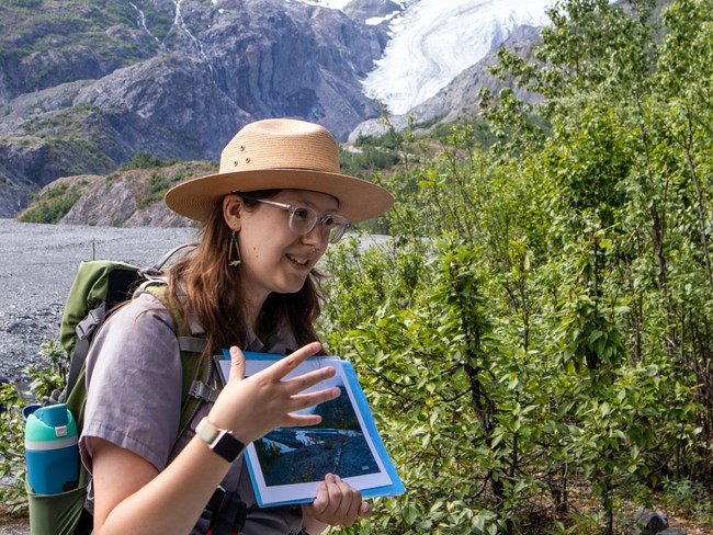A ranger holds up a photo with a glacier in the distance