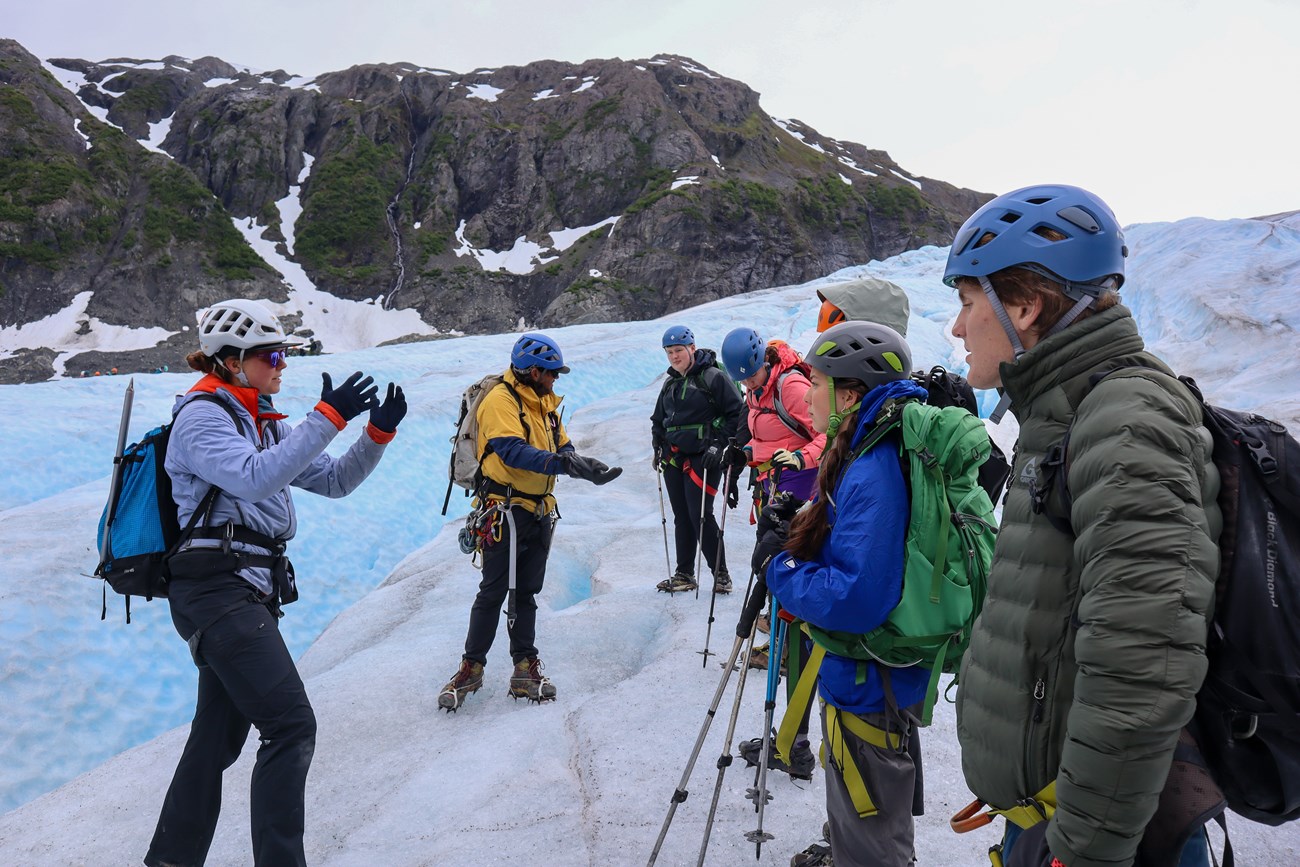 Two guides talk to a group of ice hikers in safety gear