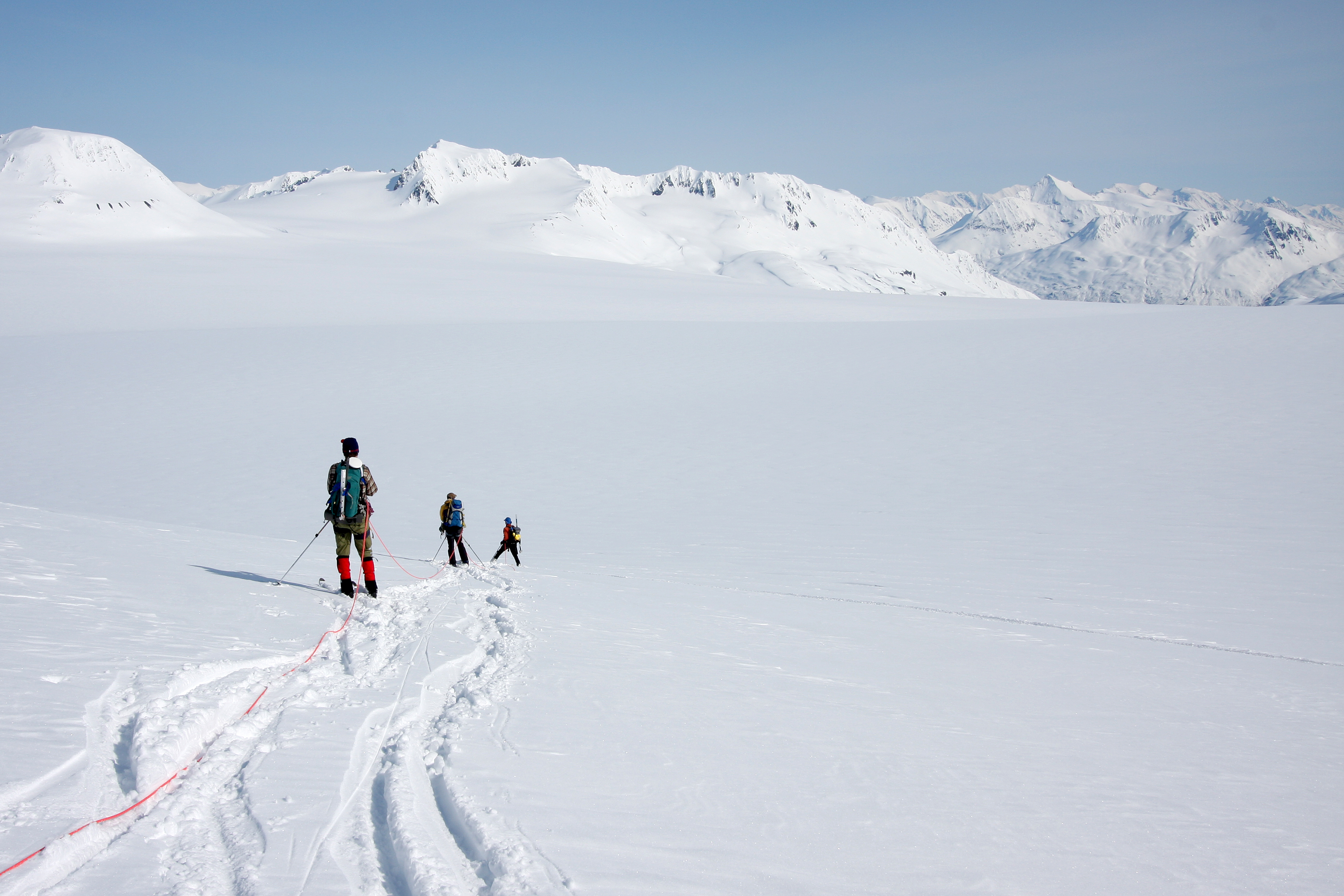 Three skiers traversing an icefield look at mountains in distance