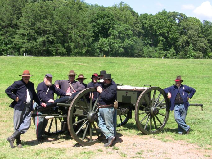 Group of volunteers dressed as Civil War soldiers stand around a cannon in a green field.