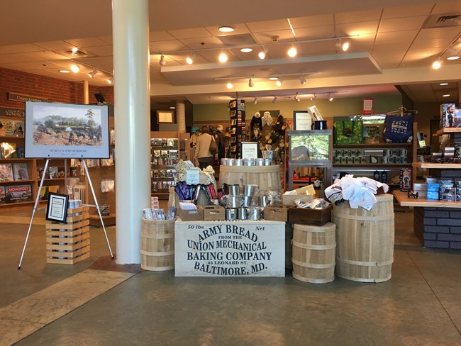 Indoor store with barrels full of items next to a sign that reads,"Army Bread from the Union Mechanical Baking Company Baltimore, MD."