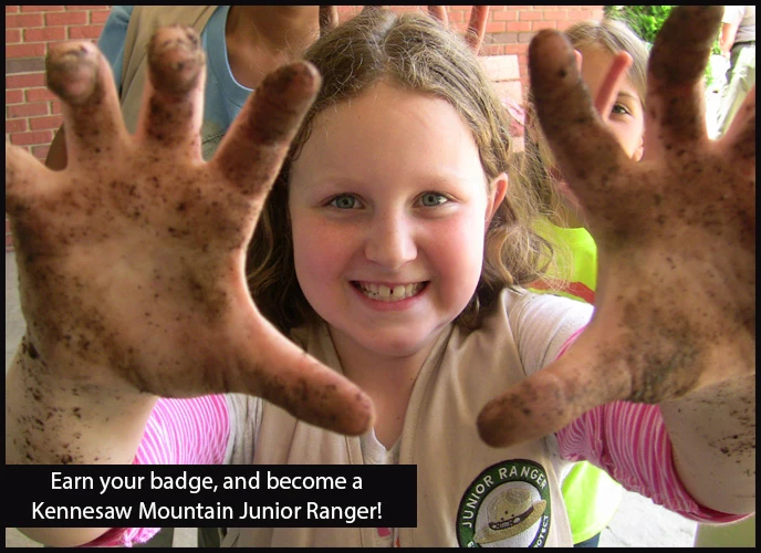 Be a Kennesaw Mountain Junior Ranger! Girl grits her teeth as she holds up her dirty hands. Text: Earn your badge, and become a Kennesaw Mountain Junior Ranger!