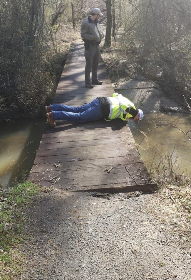 Small foot bridge over a swollen creek with two men on top of it.