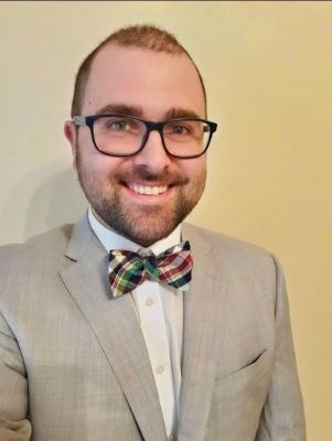 Man wearing glasses and bowtie smiles for portrait.