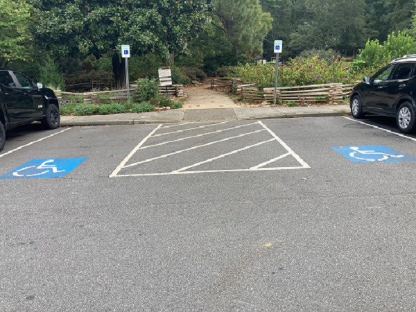 2 wide parking spaces outlined by white lines and blue signs sit on either side of entrance to a dirt trail.