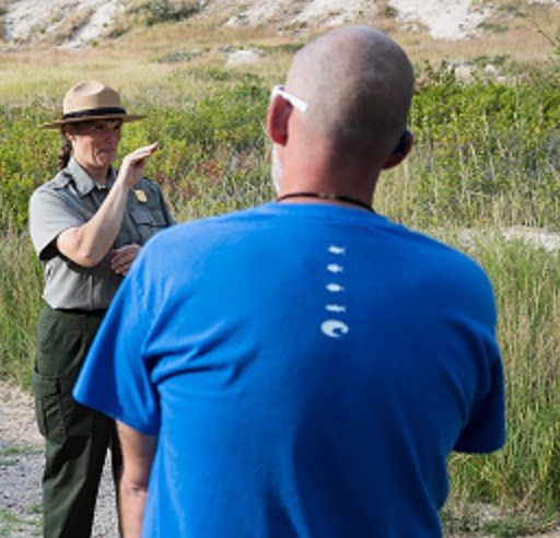 Ranger in NPS uniform signs ASL for a visitor outside.