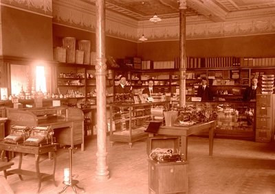 Four men stand behind a counter ready to sell goods at a historical printing store.