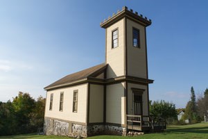 A brown exterior building with a short steeple surrounded by grass.