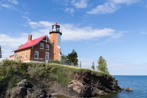 A lighthouse sits on land near the edge of a large lake.