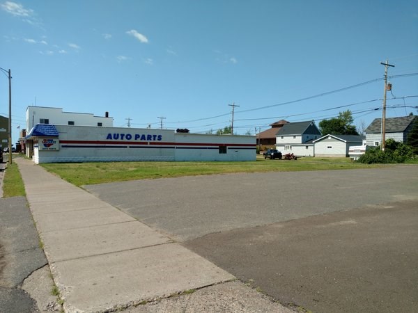 An area of grass has a building on one side and a parking lot on the other.