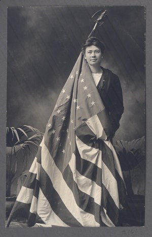 A woman poses for a photo holding an American flag that is partially draped around her body.