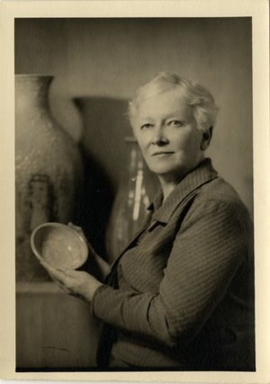 A woman slightly smiles while holding up a bowl.