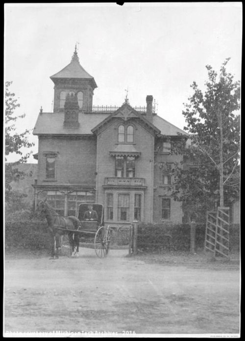 A two-story Victorian-era home with a horse and buggy in front of it.