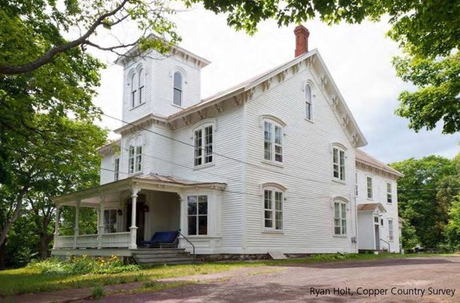 A two-story house with a steeple, white siding, and many windows.