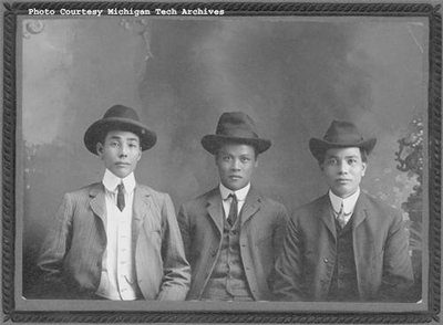 Three men with hats on sit down and pose for a photograph.