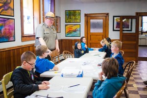A standing park ranger talks to a group of students seated at three tables.