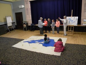 A group of students sit or stand on a map of Lake Superior.