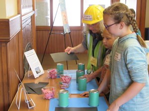 A woman with a hard hat on shows two students photographs.