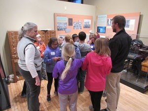 A group of students look at a museum exhibit with adults.