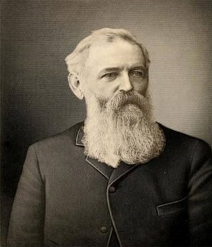 A man with a beard poses for a photograph from the chest up.