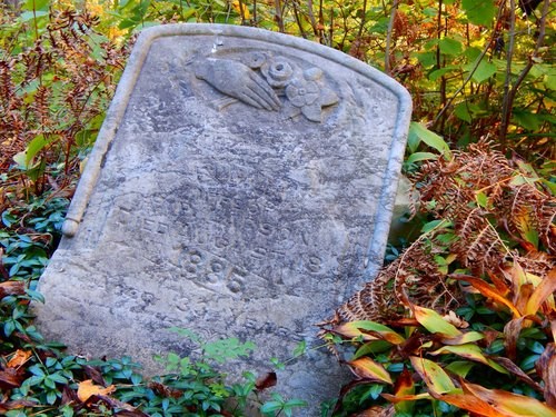 An old grave marker with a barely readable engraving sits in the grass.