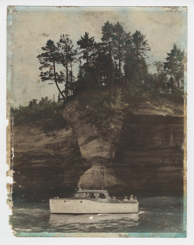In this historic photograph from the Pictured Rocks National Lakeshore archives, tourists are seen viewing the Flower Vase rock formation, ca. 1960.