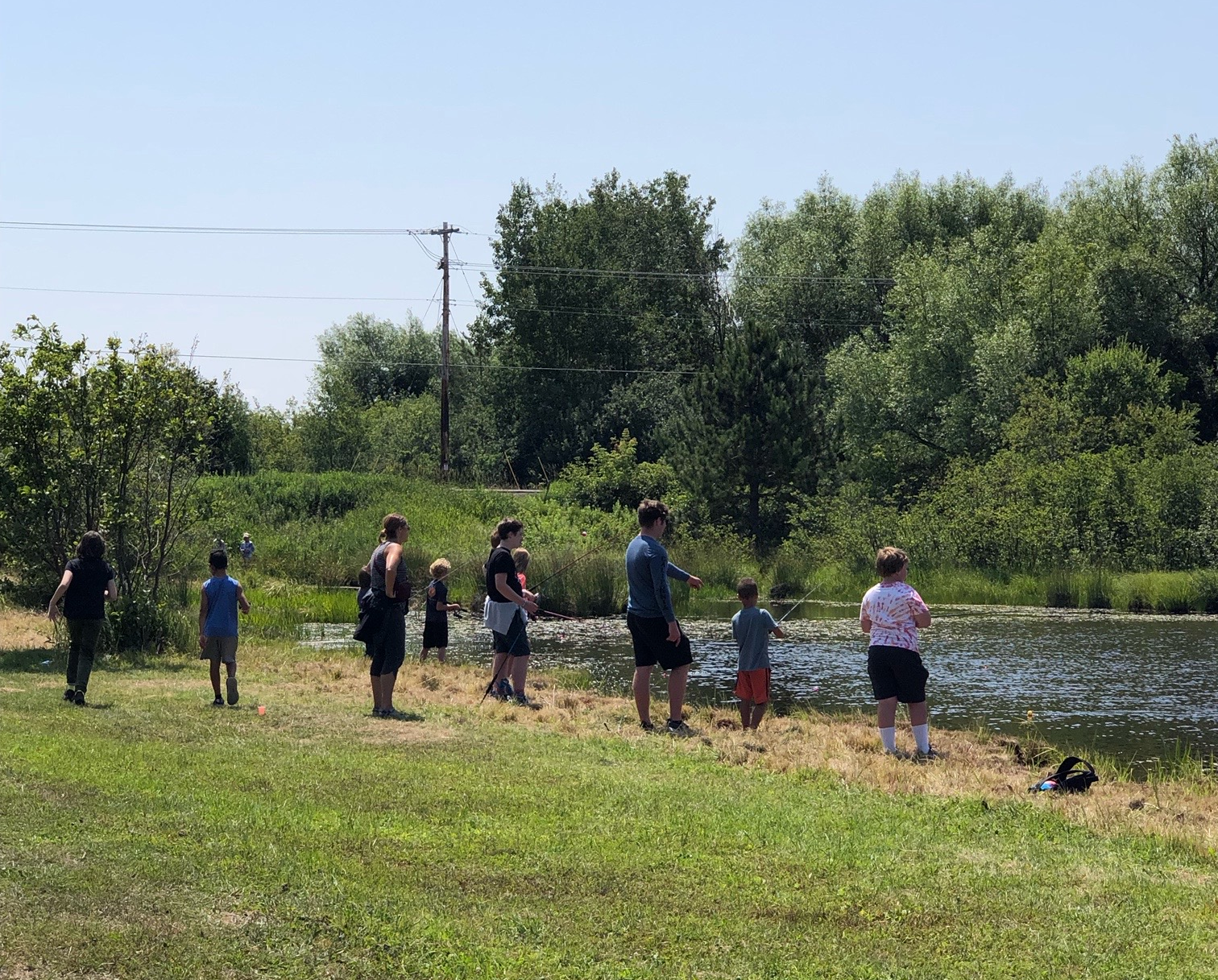 Children fishing on a small pond surrounded by grass and trees