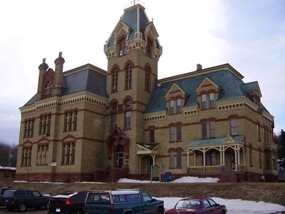 A large courthouse is surrounded by a parking lot and vehicles.