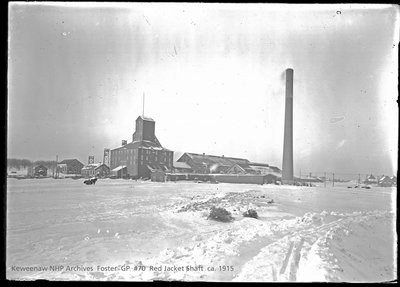 A copper mining location with a collection of buildings  and a smokestack in the winter.