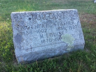 A grave marker lays on top of the grass in a cemetery.