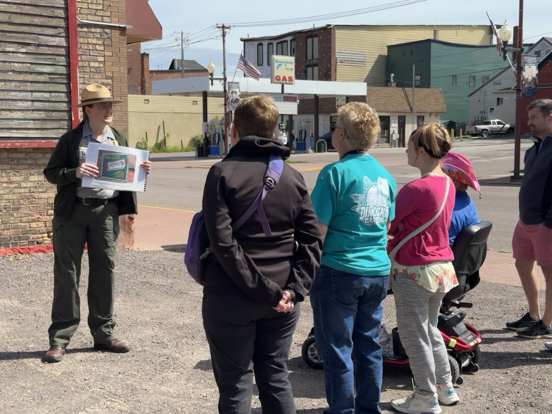Ranger Program - Ghost Signs A park ranger holding a photograph stands in front of a group gathered on the sidewalk near a historic sign